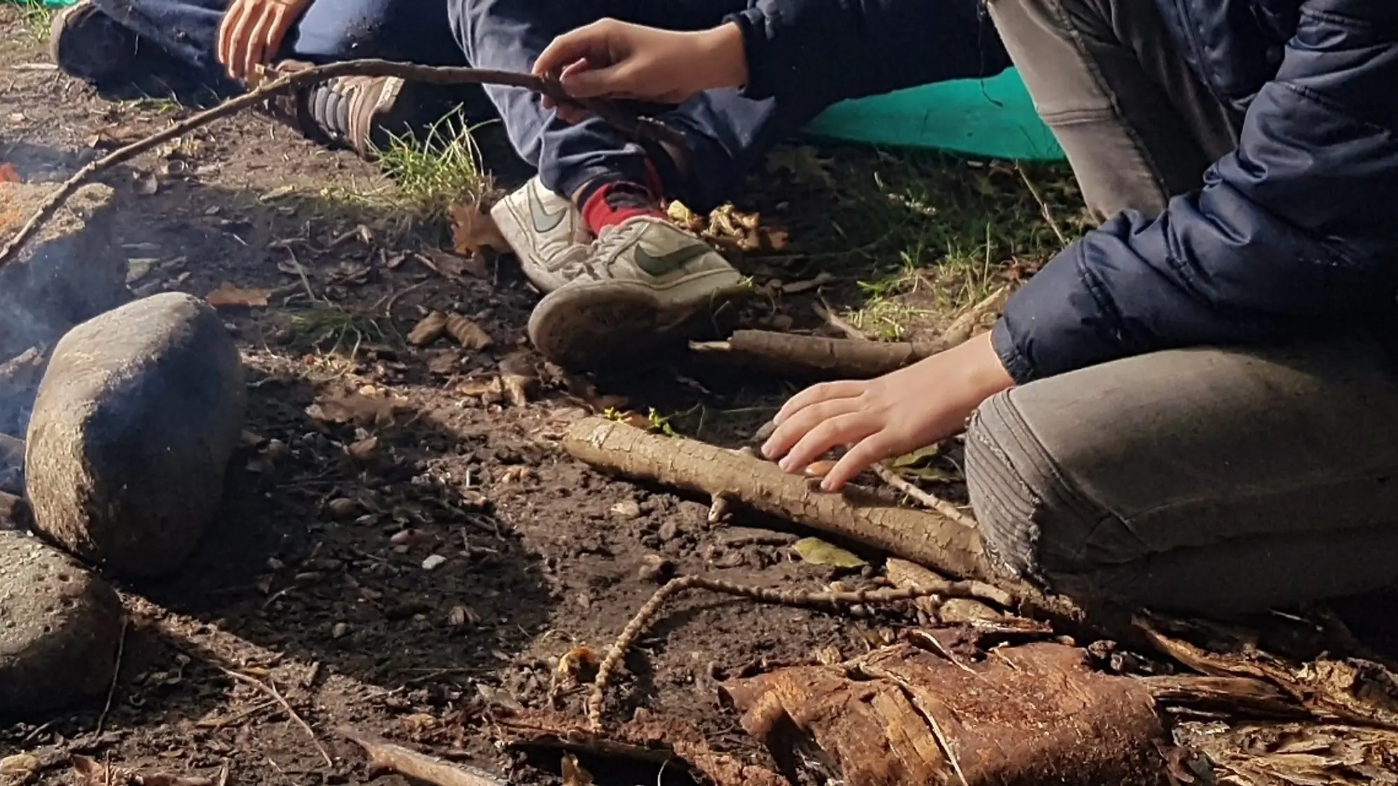Hände und Stöcke an einem kleinen Lagerfeuer im Wald.