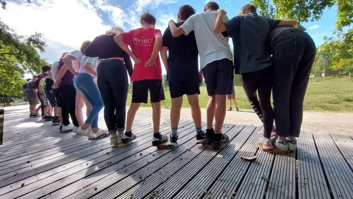 Jugendliche stehen eng Arm in Arm auf einem Steg, von hinten fotografiert.