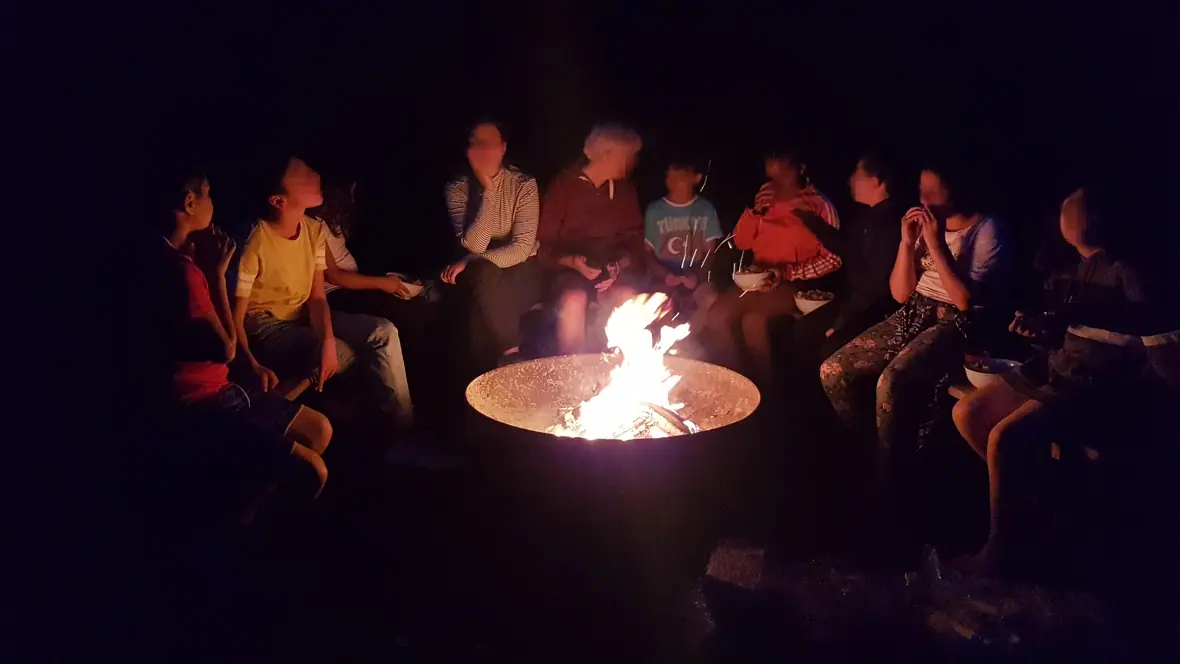 Eine Gruppe sitzt abends um eine Feuerschale beim Lagerfeuer.