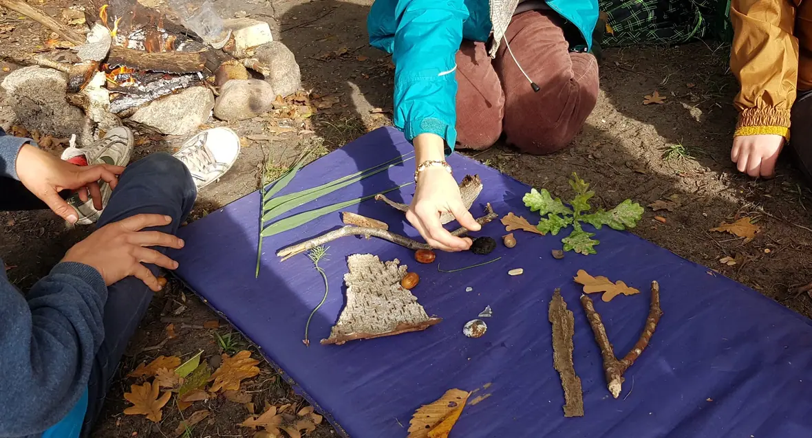 Ein Naturmandala aus Rinde, Blättern, Stöcken und Steinen entsteht auf einer Decke.