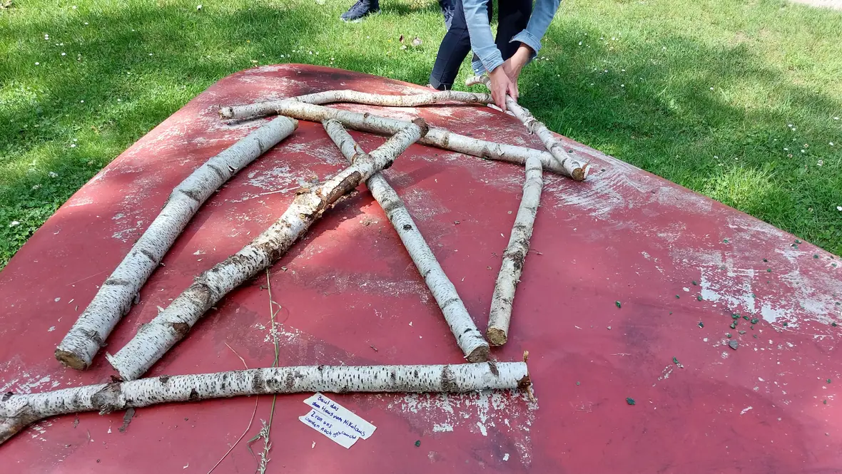 Aus Birkenstämmen gelegter Stern, eine Hand legt einen weiteren Ast an.