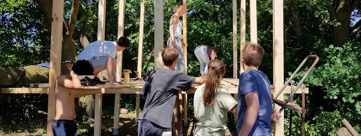 Eine Gruppe errichtet gemeinsam ein Holzgerüst in einem Waldcamp.
