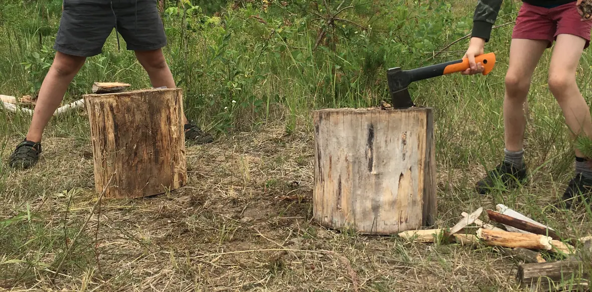 Zwei Jugendliche spalten Brennholz mit der Axt im Camp.
