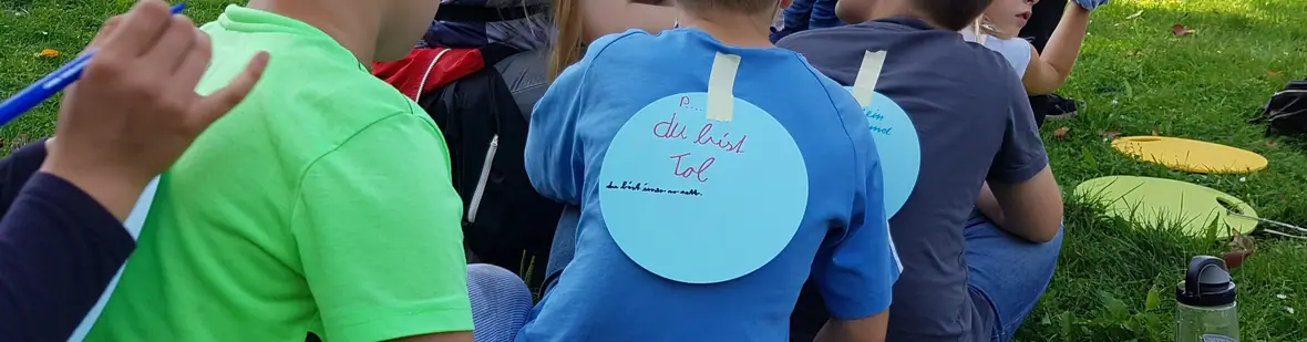 Kinder mit handgeschriebenen Wertschätzungs-Botschaften auf dem Rücken, von hinten.