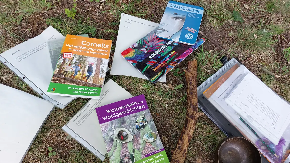Naturpädagogik-Materialien auf dem Waldboden: Bücher, Klangschalen und Stifte.