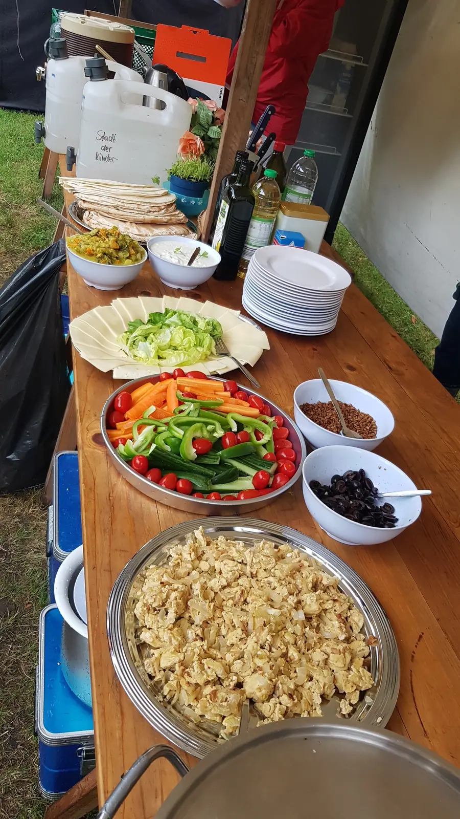 Ein selbst gemachtes Buffet mit Gemüse, Fladenbrot und Dips auf einem Holztisch im Freien.