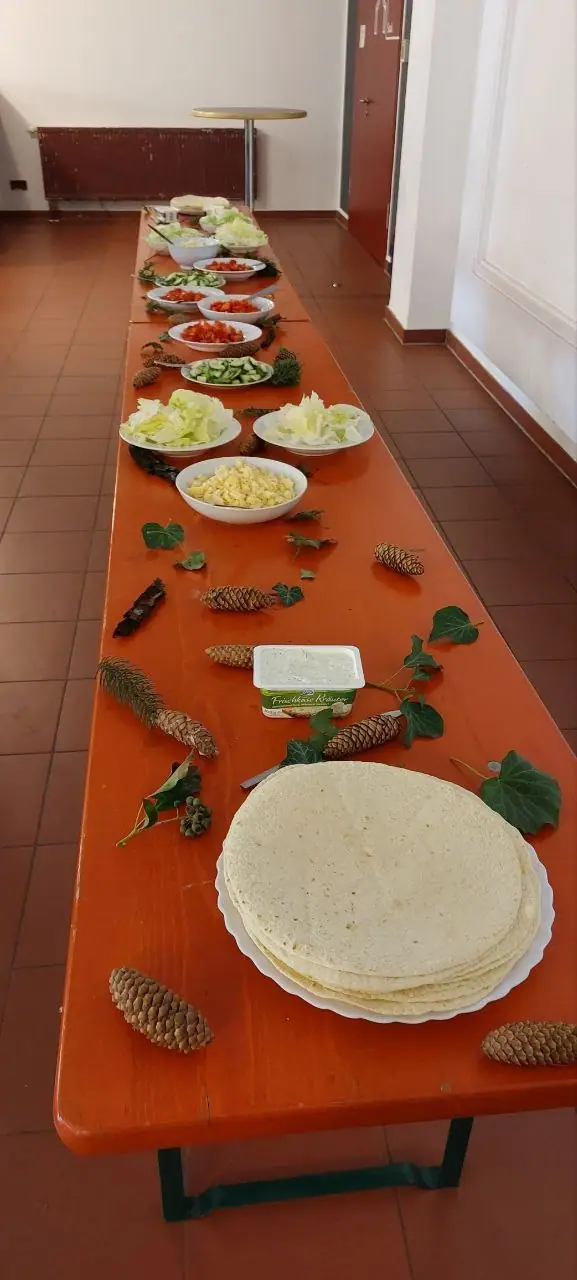 Eine lange Tafel mit vorbereitetem Wrap-Buffet, dekoriert mit Zapfen und Efeu.