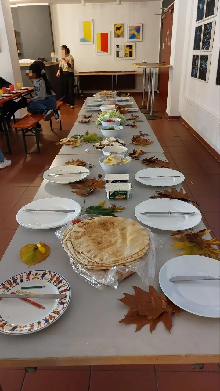 Eine lang gedeckte Tafel mit Fladenbrot und Buffet in einem Gruppenraum.